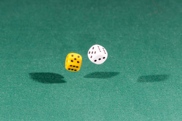 Two white and yellow dices falling on a green table