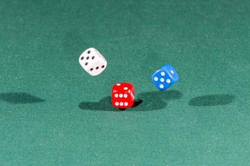 White, red and blue dices falling on a green table