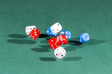 White, red and blue dices falling on a green table