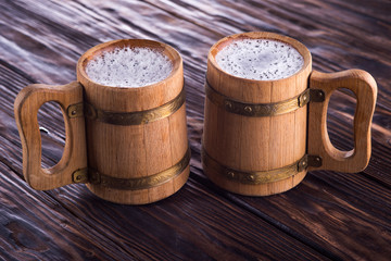Two oak mugs with beer inside. On dark wooden background
