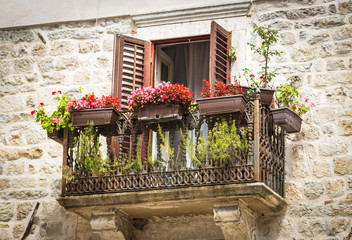 Beautiful vintage balcony with openwork metal railings, decorated with red flowers in Kotor,...