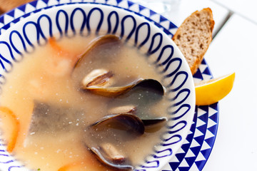 Seafood soup with mussels, prawns and fish in white bowl with blue ornament in restaurant.