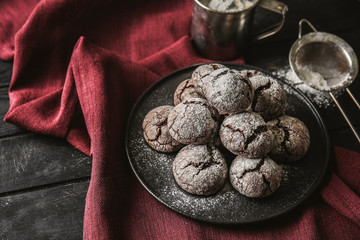 Plate with tasty chocolate cookies and sugar powder on table