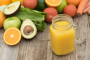 Fruit juice in the glass jar. Green background, wooden table. Fresh vegetables and fruits - avocado, apple, tomatoes. . Healthy, vegan food and drinks.