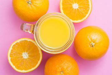 Colorful composition with mason jar glass full of fresh orange juice with straw, fruit, isolated on pink background. Close up, copy space, top view.