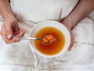 Heilfasten, Kur - Mann mit einem Teller Suppe in der Hand im Bett