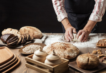 Hands of caucasian man prepares pastry by himself, close up. Man kneads dough on wooden counter with flour and rolling pin, baking organic bread or delicious bun.