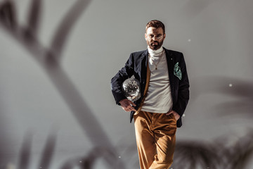 selective focus of bearded man holding mosaic disco ball and looking at camera on grey background