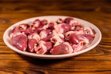 Ceramic plate with raw chicken hearts on wooden table