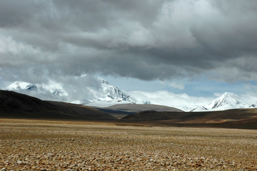 Naklejka premium Tibetan valley with snow-capped mountains and low-hanging clouds