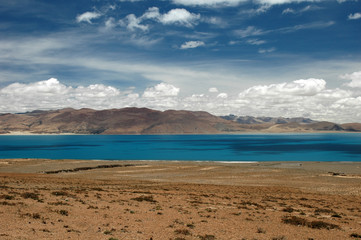 Lake with turquoise water in Tibet against the backdrop of mountains and clouds