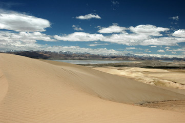 Fototapeta na wymiar Sandy hills, lake, blue sky and clouds in a Tibetan landscape