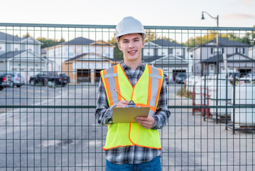 Happy young construction worker wearing safety gear and holding a clipboard.