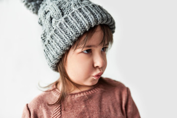 Beautiful little girl with blowing kiss in the winter warm gray hat, wearing sweater isolated on a white studio background.