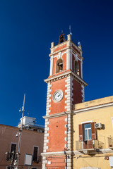 Clock tower, red with white bricks. The building dates back to the nineteenth century. Iron street lamp in liberty style. Cerignola, Puglia, Italy. Surveillance cameras.