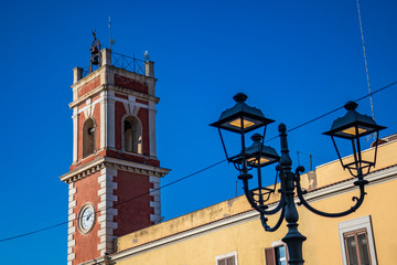 Clock tower, red with white bricks. The building dates back to the nineteenth century. Iron street lamp in liberty style. Cerignola, Puglia, Italy.