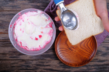 Boy hand with scoop takes ice cream and serving in a bread over an  old tabletop.