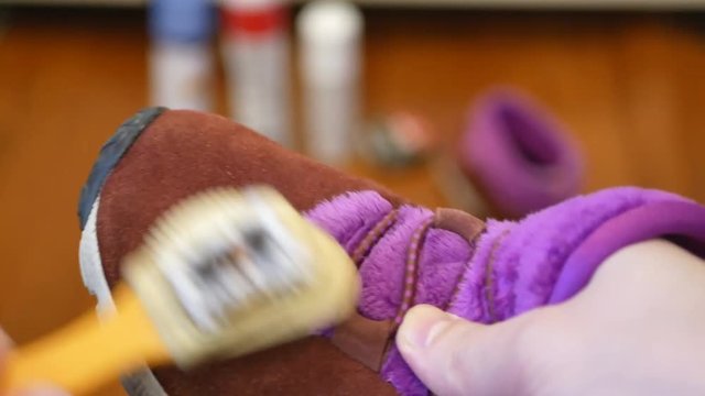 man cleaning suede vivid burgundy red and pink shoes with special brush. blurred care product set on background. closeup 4k footage