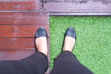 Woman feet wearing black shoes on a green grass and wooden background.