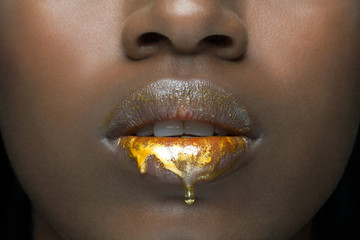 Close up of a beautiful, young, black woman's lips with golden, liquid make up dripping down her lips.