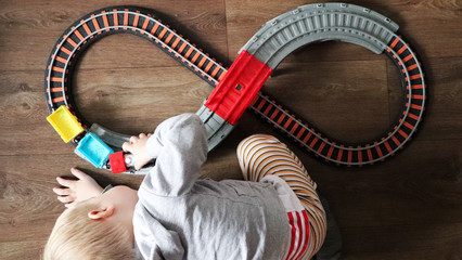 A little boy plays a children's railway. Mom is watching her son from above. The child is fascinated by the train
