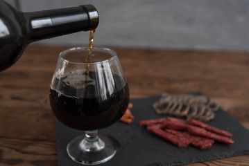 Red granat wine pouring from the bottle into wine glass, close-up 