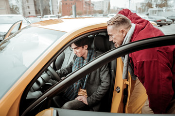 Young son sitting in new car with his father standing nearby