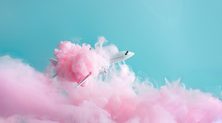Passenger jet airplane flying through pastel pink clouds. Minimal transportation, travel or vacation concept.