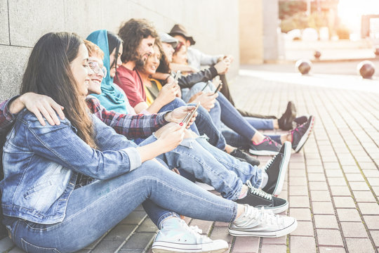 Millennial friends using smartphones sitting outdoor 