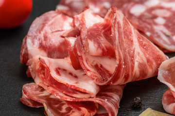 antipasto with sliced salami, cheeses, prosciutto, ham, tomato on black slate background