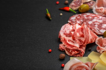 antipasti with sliced salami, cheeses, prosciutto, ham, olive on black slate background, copy space