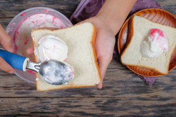 Boy hand with scoop takes ice cream and serving in a bread over an  old tabletop.