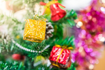 Decorated Christmas tree with fake snow spray closeup. Golden red gift box ,red bell and pine cones ornaments hang on christmas branch tree with bokeh and colorful ribbons background. 