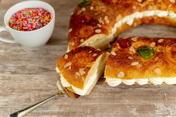 King's cake made by hand in the oven, on a cozy wooden base, and a cup with colorful chocolate topping.