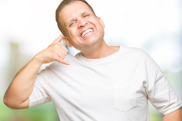 Middle age arab man wearig white t-shirt over isolated background smiling doing phone gesture with hand and fingers like talking on the telephone. Communicating concepts.