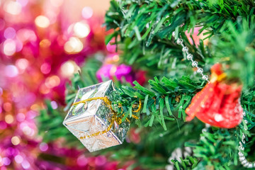 Decorated Christmas tree with fake snow spray closeup. Silver gift box ornaments hang on christmas branch tree with bokeh and colorful ribbons background. Merry christmas and happy new year concept.