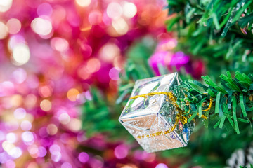 Decorated Christmas tree with fake snow spray closeup. Silver gift box ornaments hang on christmas branch tree with bokeh and colorful ribbons background. Merry christmas and happy new year concept.