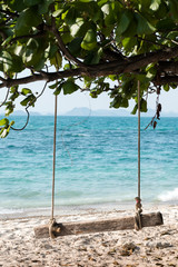Empty wooden swing on an exotic beach - Ko Kham island, Thailand, Andaman Sea. Wodden swing tied with ropes to a tree with sea in the background.