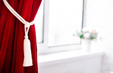 The claret curtain collected by a decorative lace near a window.
