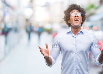 Afro american business man wearing glasses over isolated background crazy and mad shouting and...
