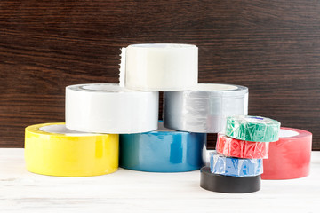 Several rolls of duct tape stacked in a pyramid. stack of electrical tape stand nearby. have toning. shallow depth of cut