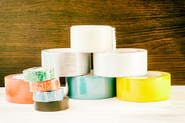 Several rolls of duct tape stacked in a pyramid. stack of electrical tape stand nearby. have...