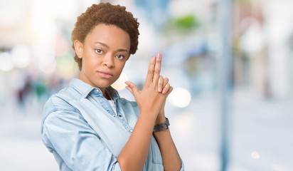Young beautiful african american woman over isolated background Holding symbolic gun with hand gesture, playing killing shooting weapons, angry face