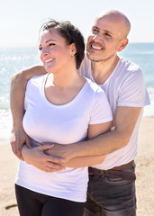 elderly man with a woman in white shirts cuddling on sand on beach