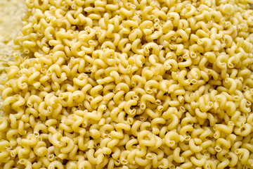 Yellow dry uncooked cellentani pasta, texture background, top view