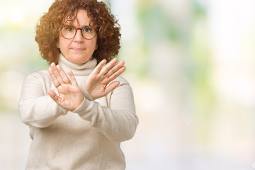 Beautiful middle ager senior woman wearing turtleneck sweater and glasses over isolated background Rejection expression crossing arms and palms doing negative sign, angry face