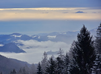 Naklejka na ściany i meble Beautiful winter landscape in Slovenia with fog in the valley. In the distance you can see church with two bell towers.
