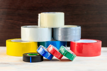 Several rolls of duct tape stacked in a pyramid. stack of electrical tape stand nearby. have toning. shallow depth of cut