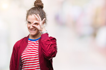 Beautiful brunette curly hair young girl wearing a jacket over isolated background doing ok gesture with hand smiling, eye looking through fingers with happy face.