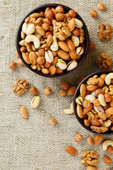 Mix of various nuts in a wooden cup against the background of fabric from burlap. Nuts as structure and background, macro. Top view.